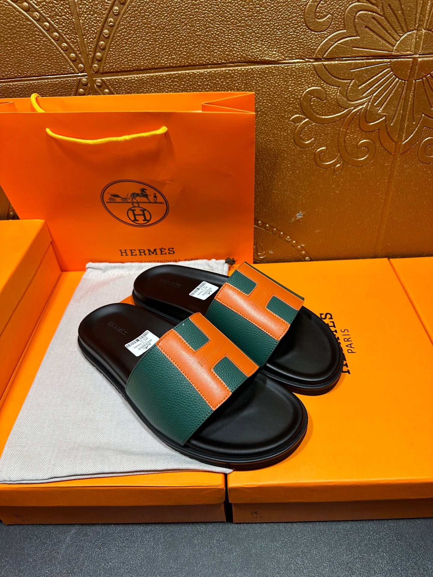 Hermes slide sandals pair with green top strap and orange H panels on black sole.