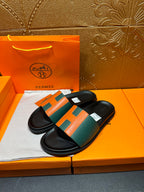 Hermes slide sandals, black slides with green and orange H over straps.