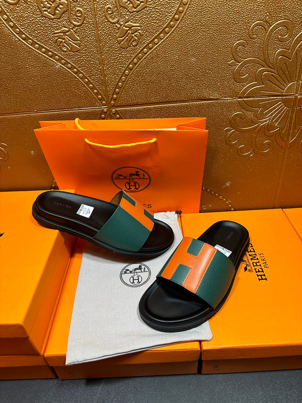 Hermes slide sandals pair on box, black soles with green and orange H straps.