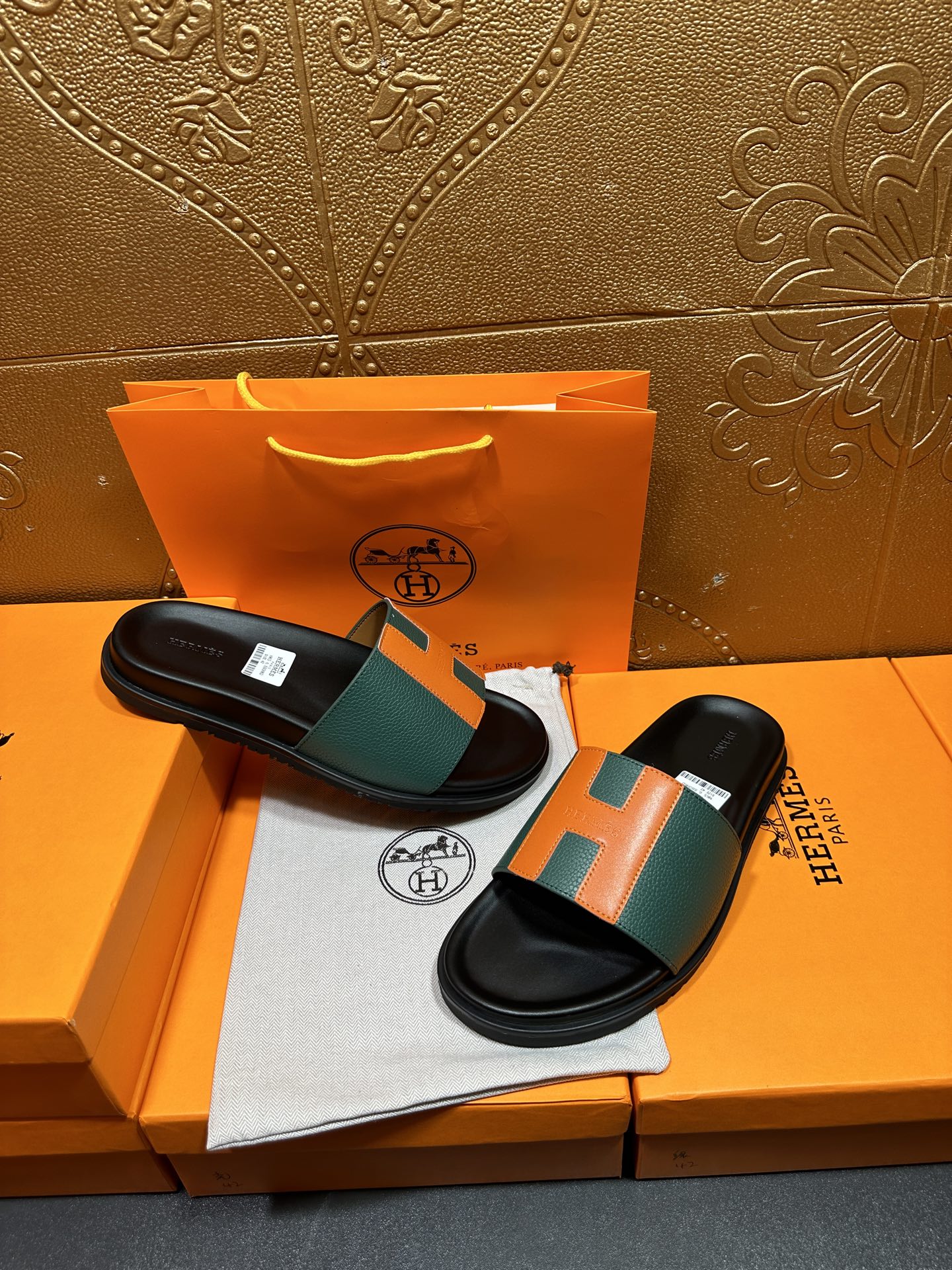 Hermes slide sandals pair on box, black soles with green and orange H straps.