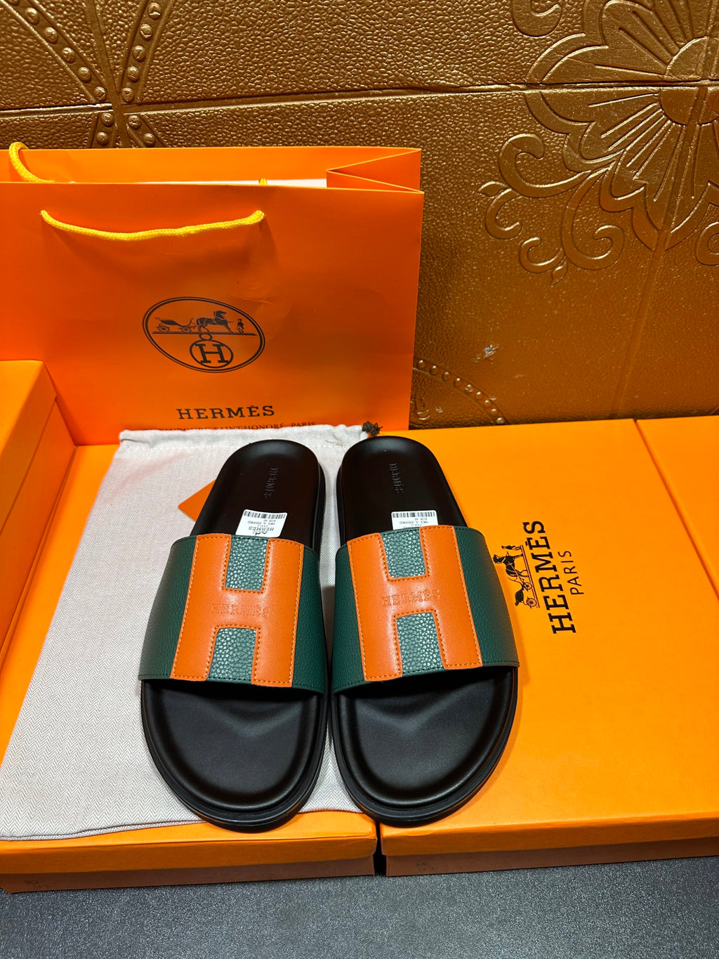 Hermes slide sandals with black footbed and green-orange H straps.