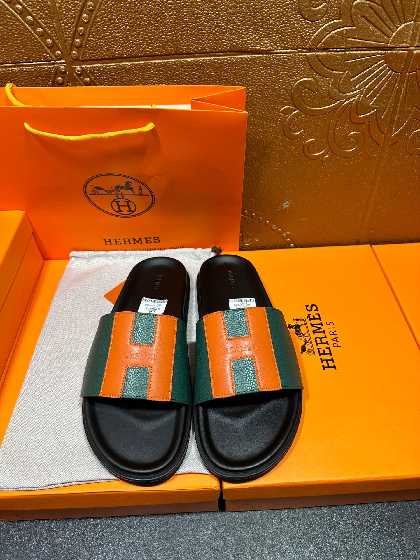 Hermes slide sandals with black footbed and green-orange H straps.