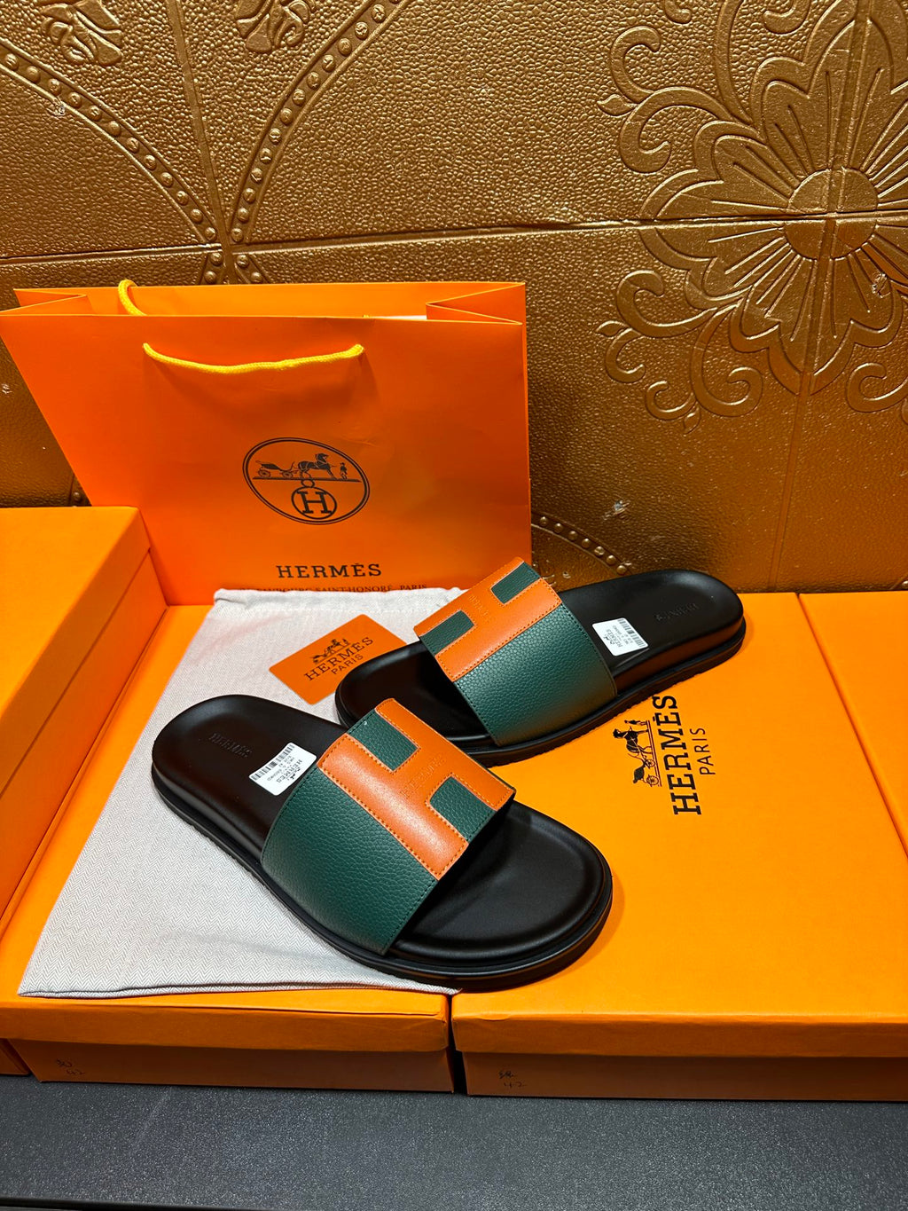 Hermes slide sandals on display, black base with green and orange strap detail.