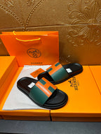 Hermes slide sandals on display, black base with green and orange strap detail.