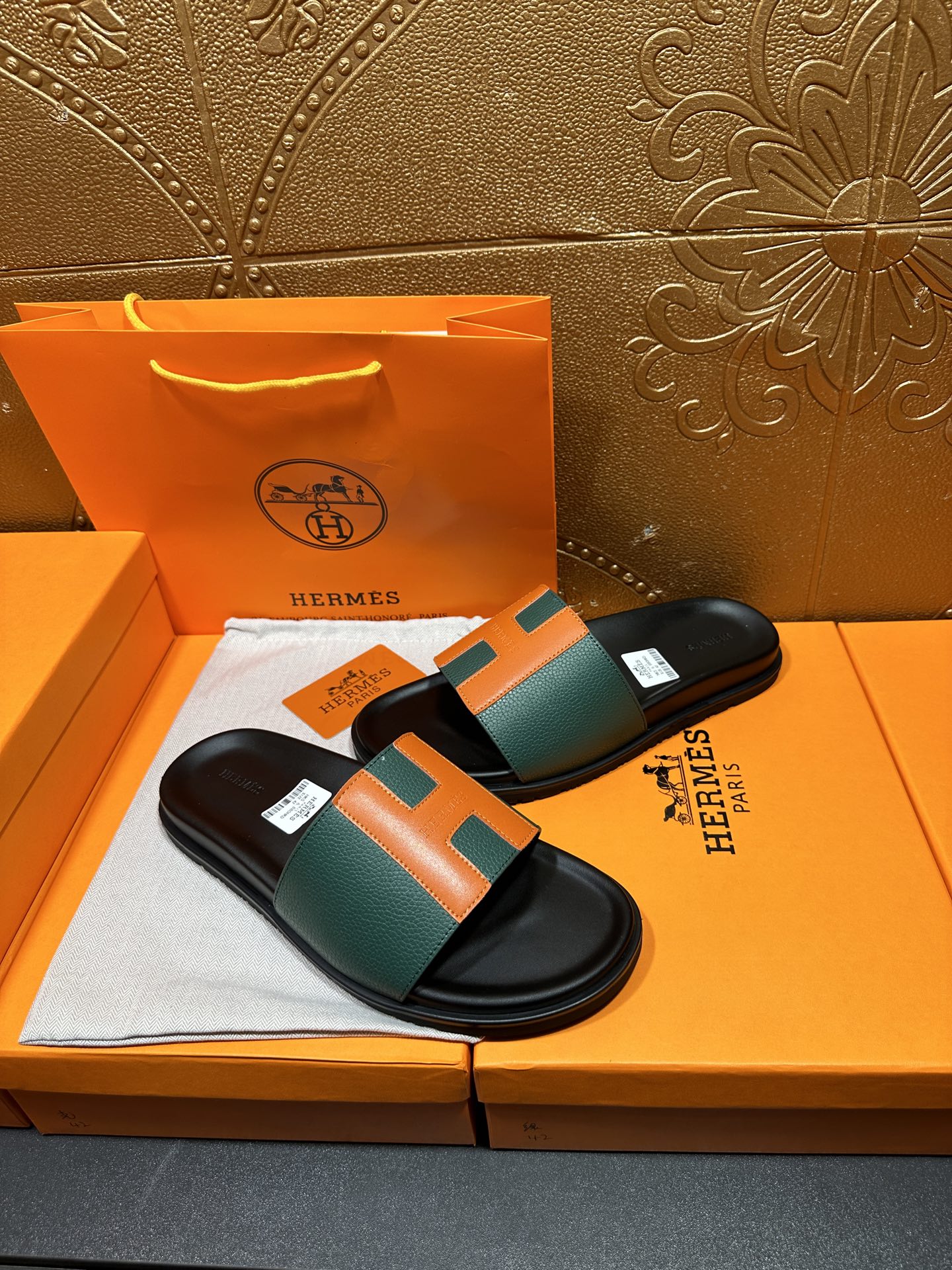 Hermes slide sandals on display, black base with green and orange strap detail.