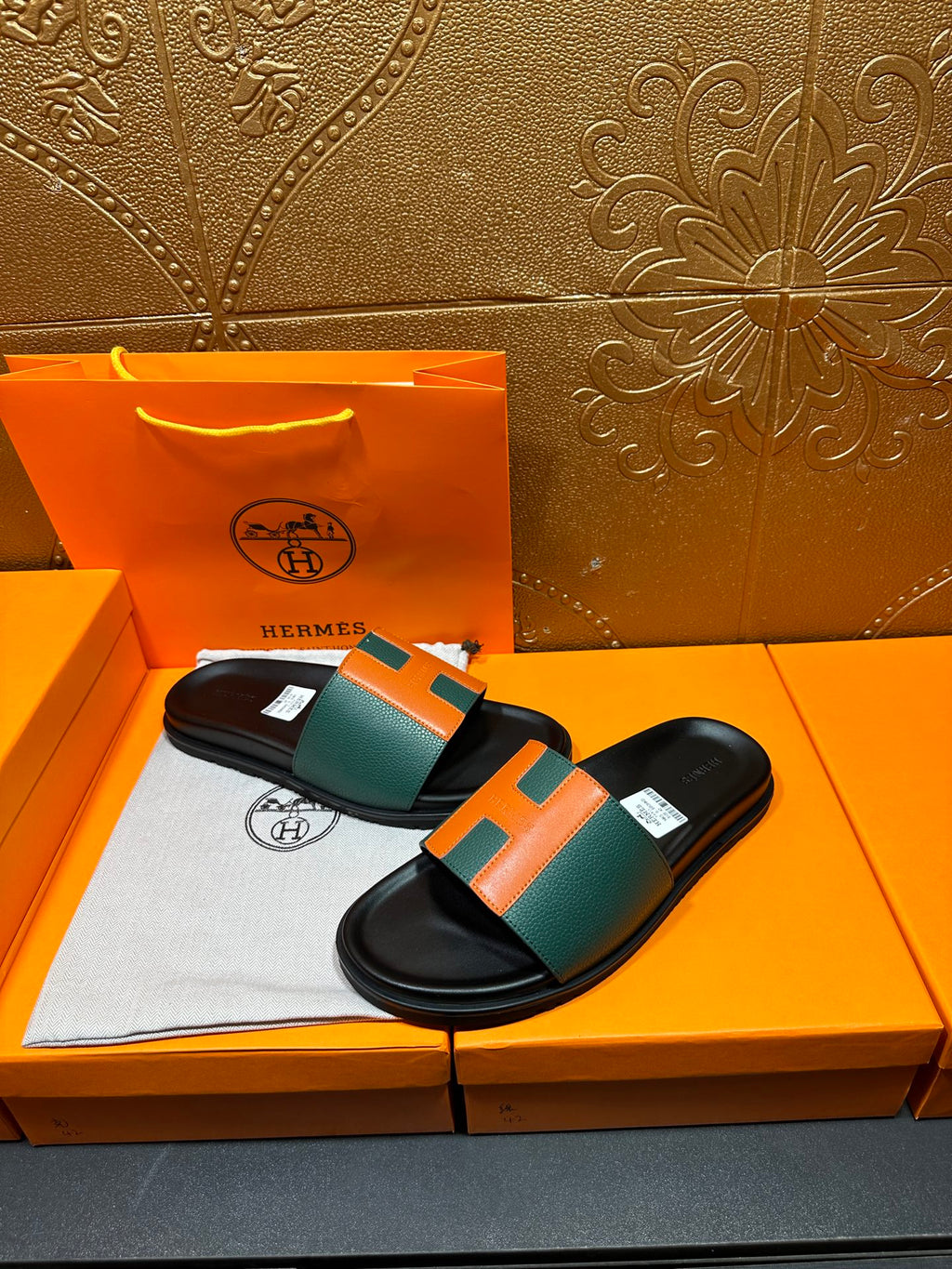 Hermes slide sandals laid flat, green-and-orange H straps on black footbeds.