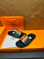 Hermes slide sandals laid flat, green-and-orange H straps on black footbeds.