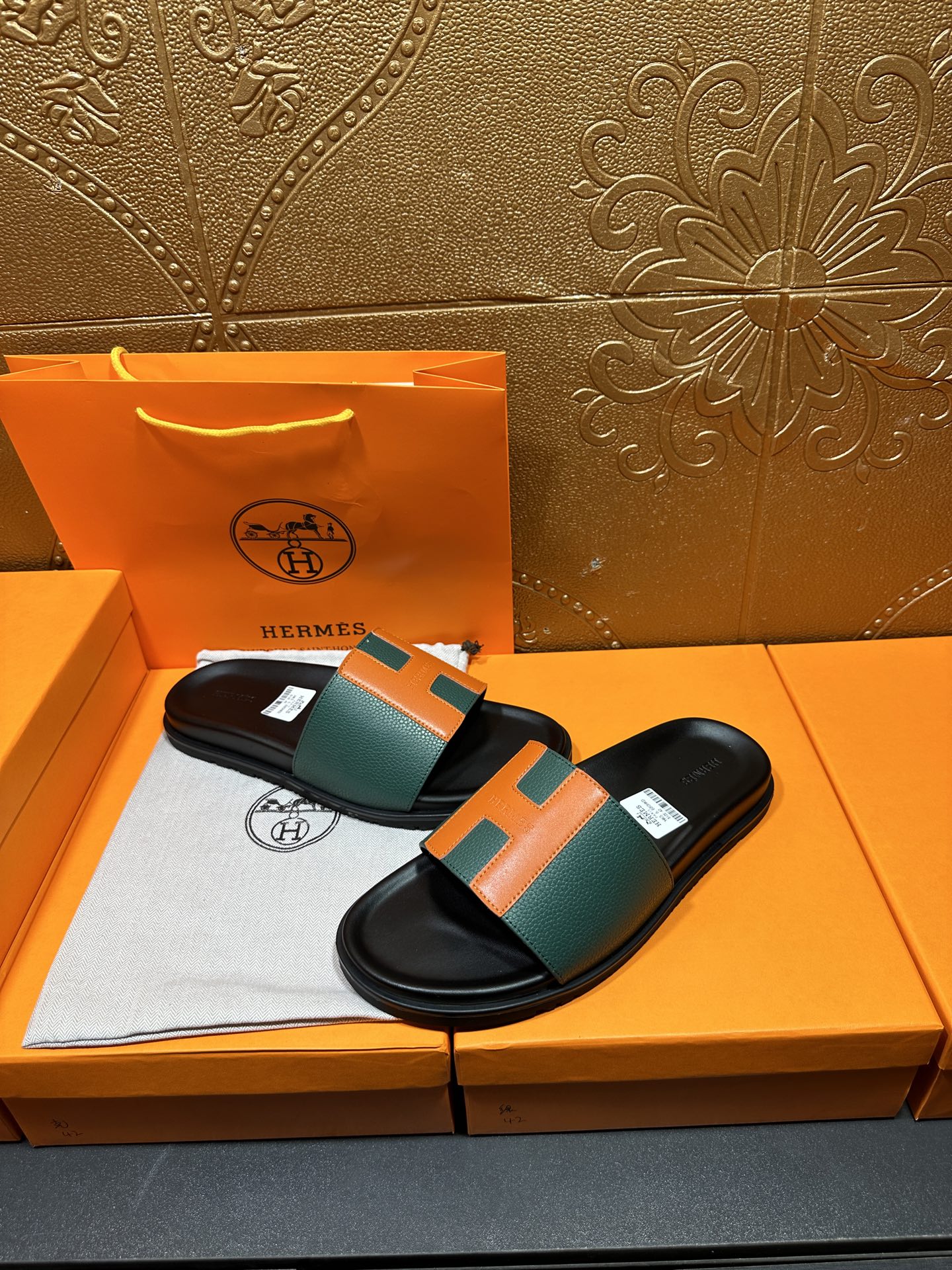 Hermes slide sandals laid flat, green-and-orange H straps on black footbeds.