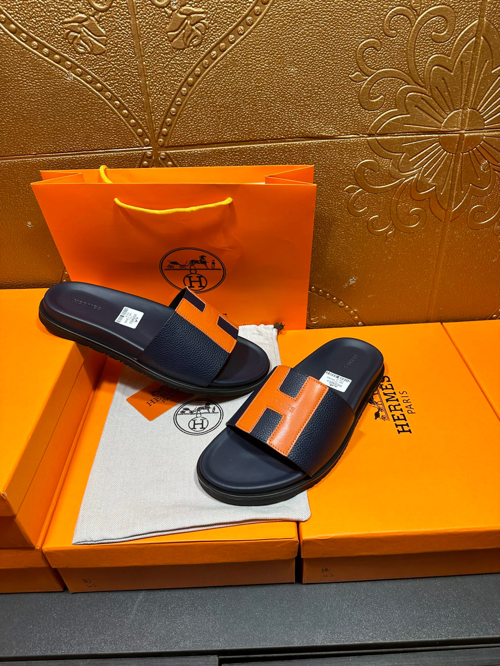 Hermes slide sandals on display, dark navy with orange H accents and cushioned footbed