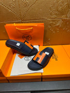 Hermes slide sandals on display, dark navy with orange H accents and cushioned footbed