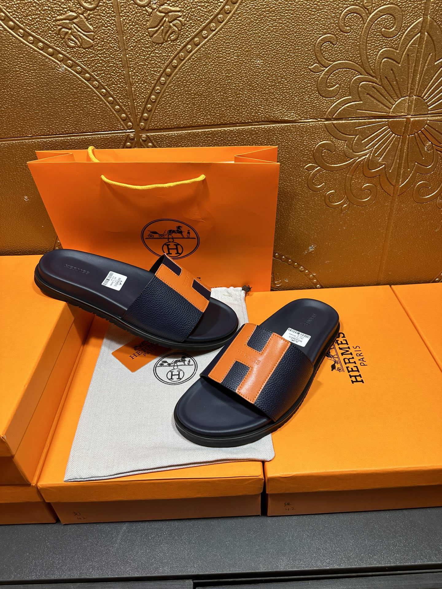 Hermes slide sandals on display, dark navy with orange H accents and cushioned footbed