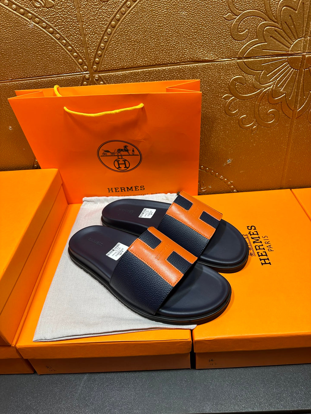 Hermes slide sandals paired, dark navy leather with orange H strap accents and flat sole