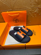 Hermes slide sandals paired, dark navy leather with orange H strap accents and flat sole