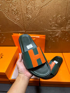Hermes slide sandal in hand, green strap with orange H pattern and black sole