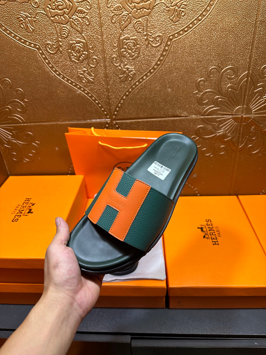 Hermes slide sandal held up, green leather with orange H detail and black base