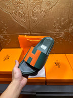 Hermes slide sandal held up, green leather with orange H detail and black base