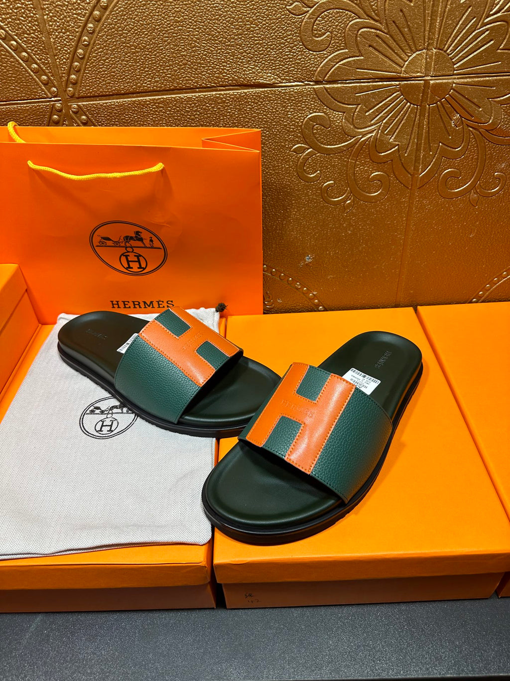 Hermes slide sandals with green and orange H straps, laid on orange shoebox