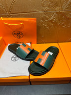 Hermes slide sandals with green and orange H straps, laid on orange shoebox