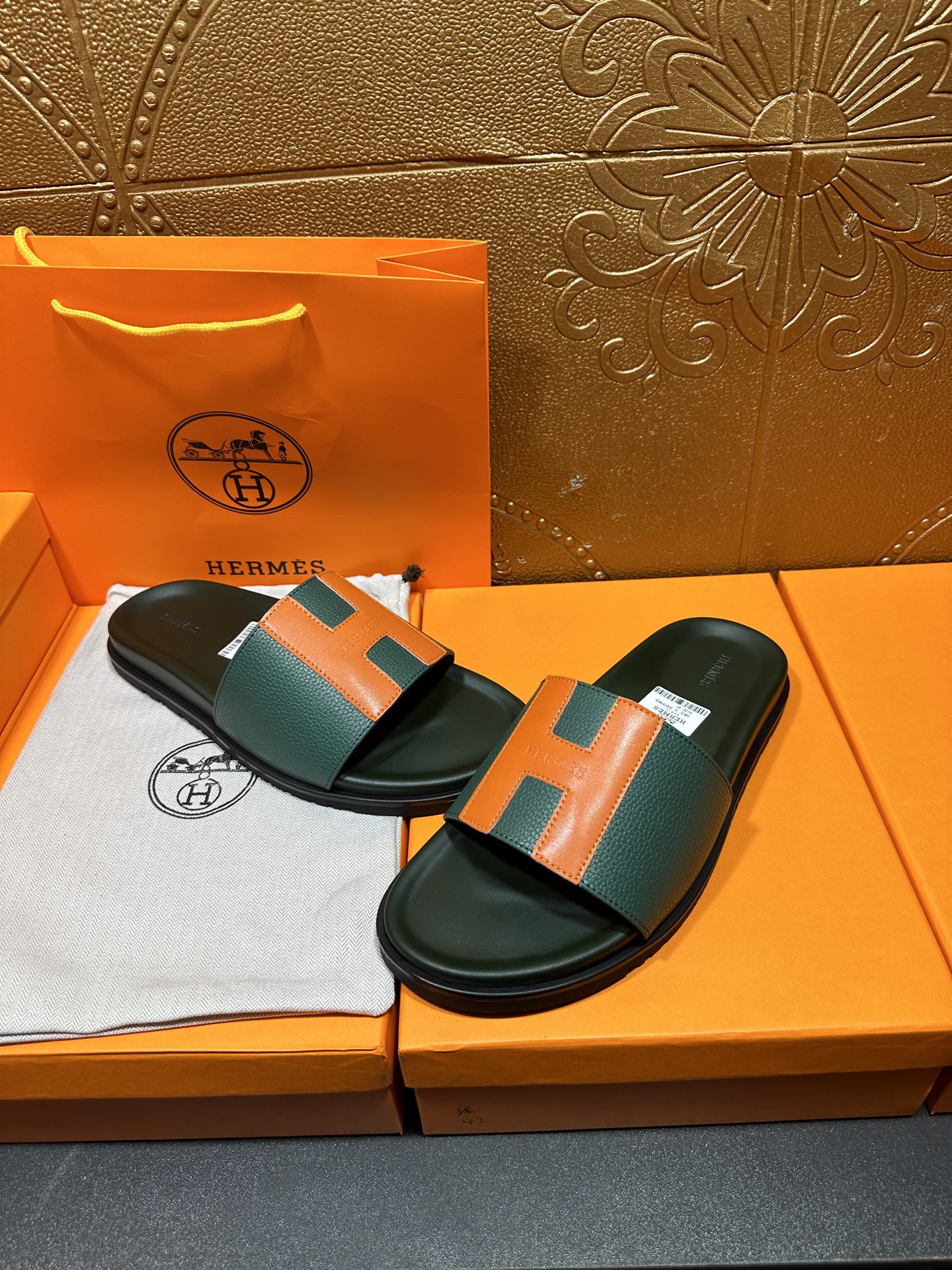 Hermes slide sandals with green and orange H straps, laid on orange shoebox