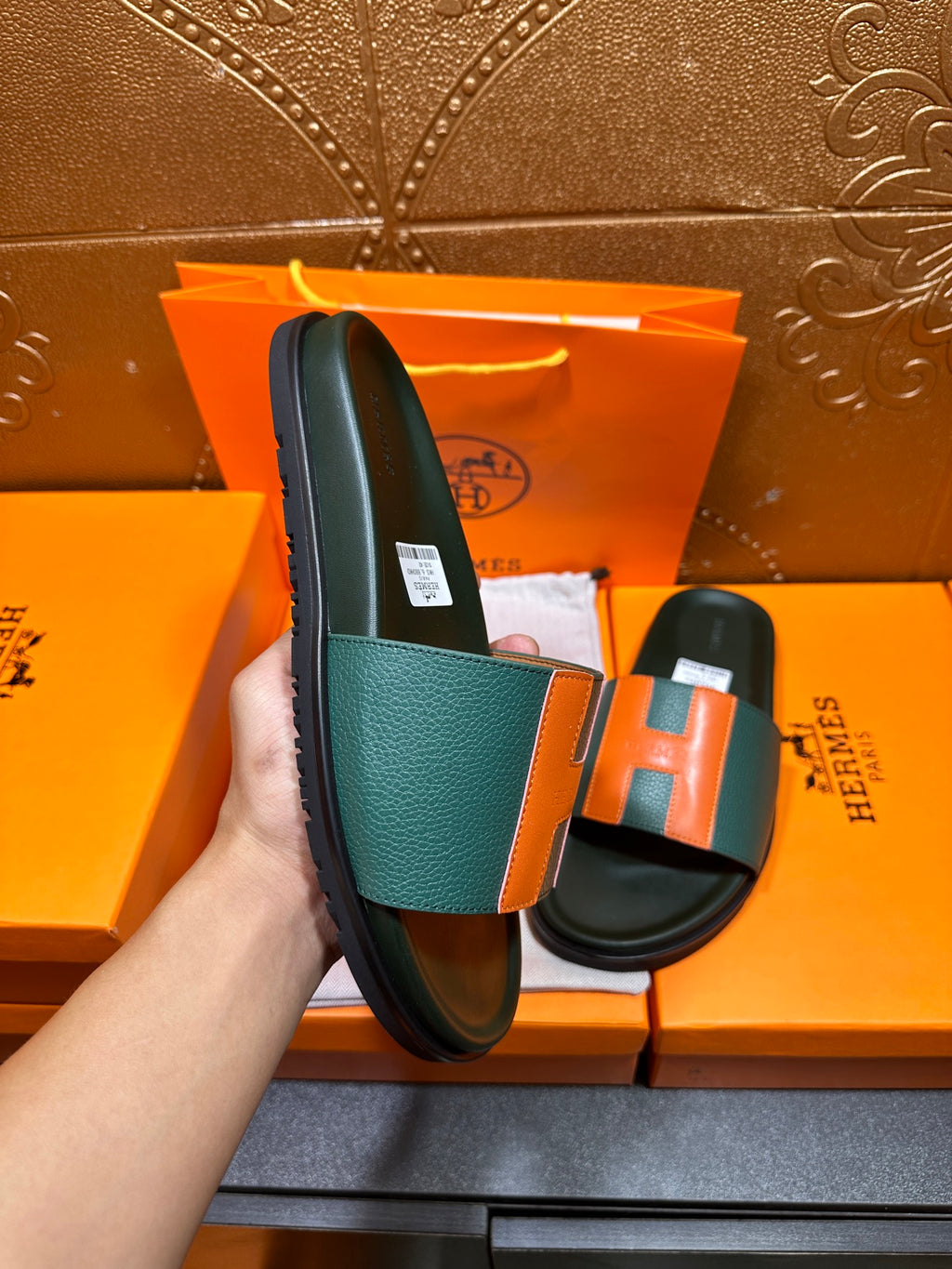 Hermes slide sandal held up, green strap and orange H detail with black sole