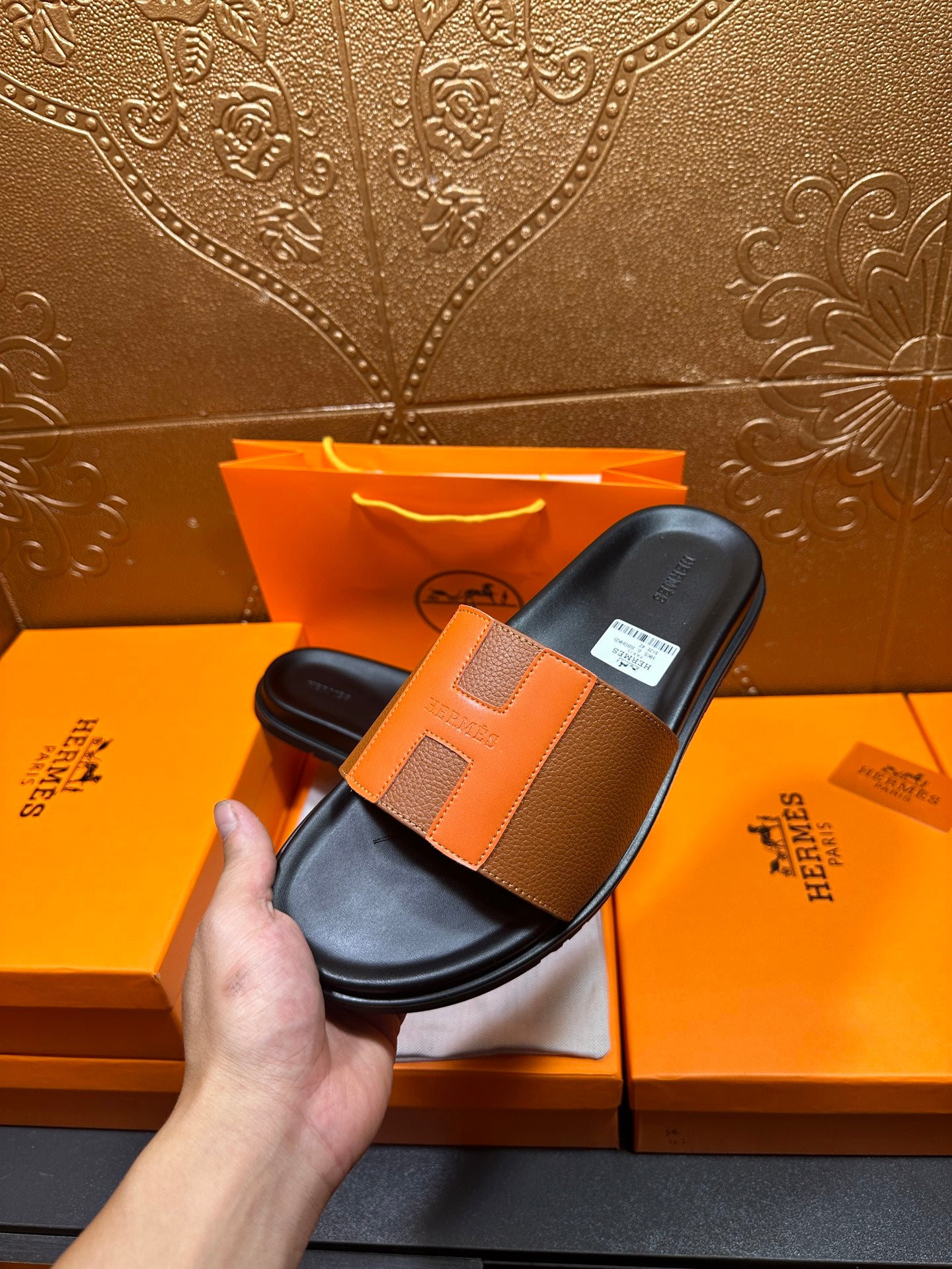 Tan leather slide sandal held in hand with black footbed and wide strap