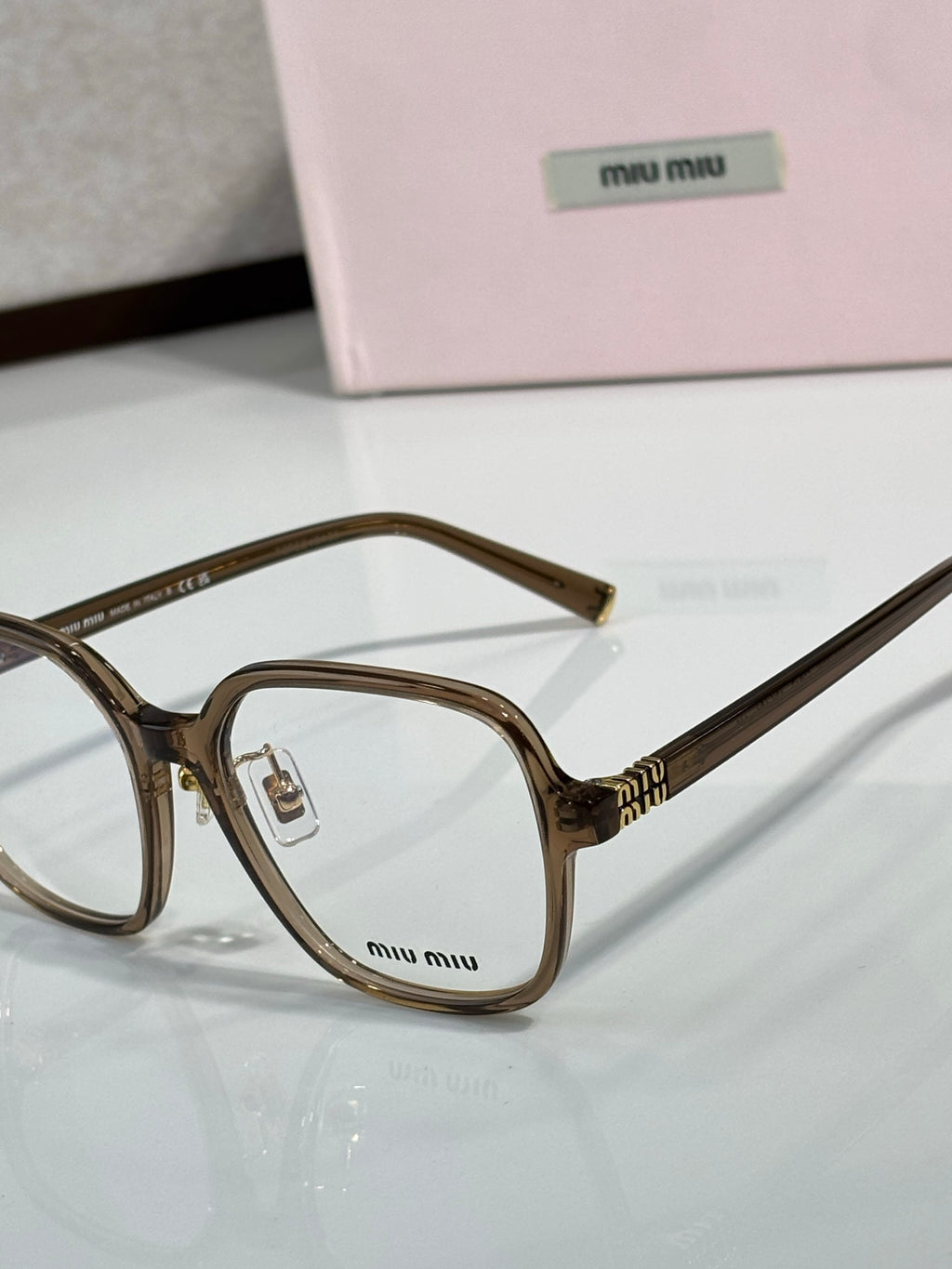 Close-up brown eyeglass frame with clear lenses and MiuMiu logo on the lens area