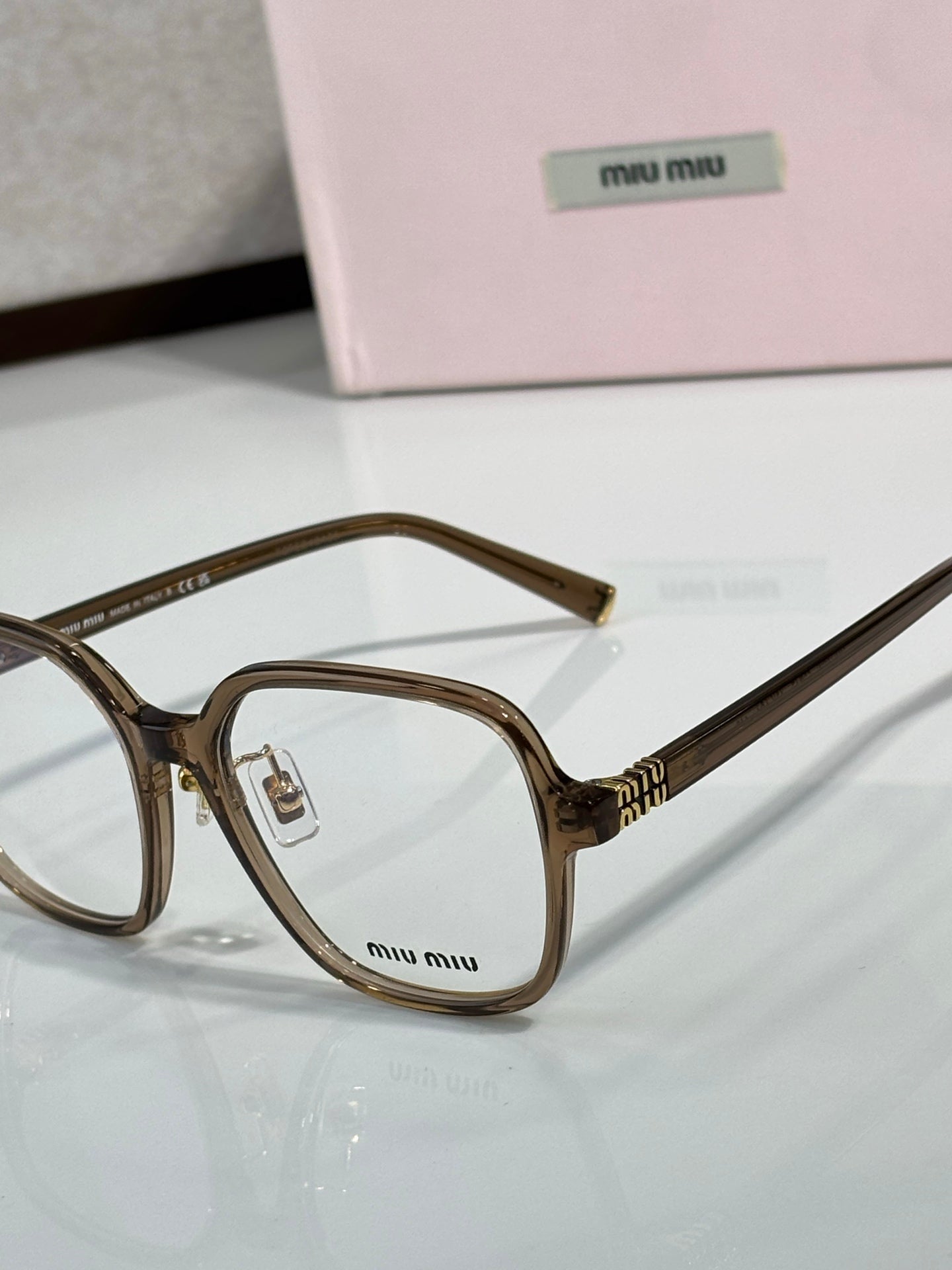 Close-up brown eyeglass frame with clear lenses and MiuMiu logo on the lens area