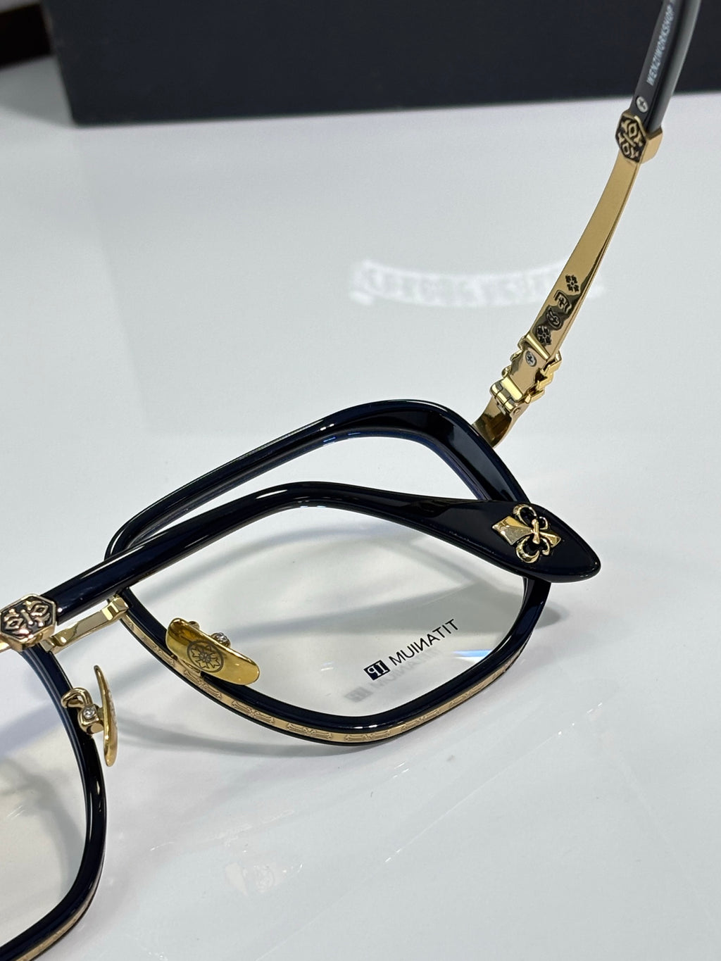 Gold-tone eyeglass frames with dark navy temples and clear lenses.