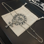 Silver-tone cross pendant necklace with chain beside beige drawstring pouch