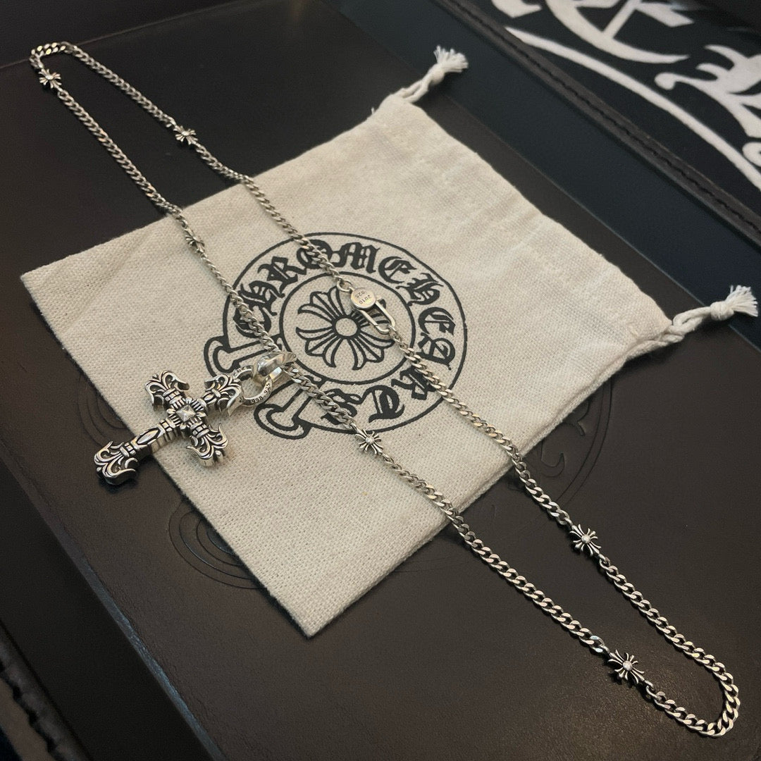 Silver-tone cross pendant necklace with chain beside beige drawstring pouch