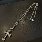 Silver-tone cross pendant necklace laid on black embossed leather surface