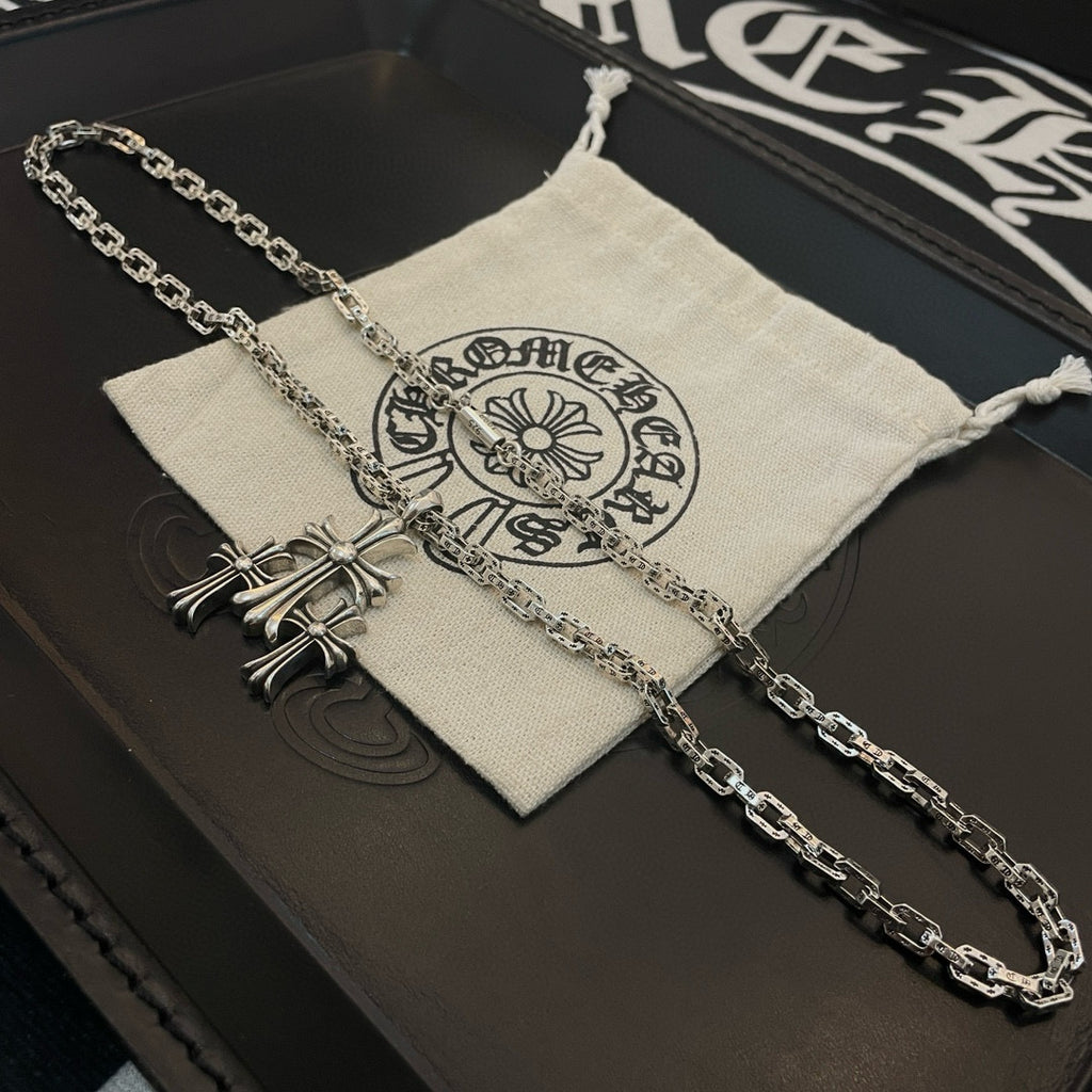 Silver cross pendant necklace draped over fabric pouch on black box