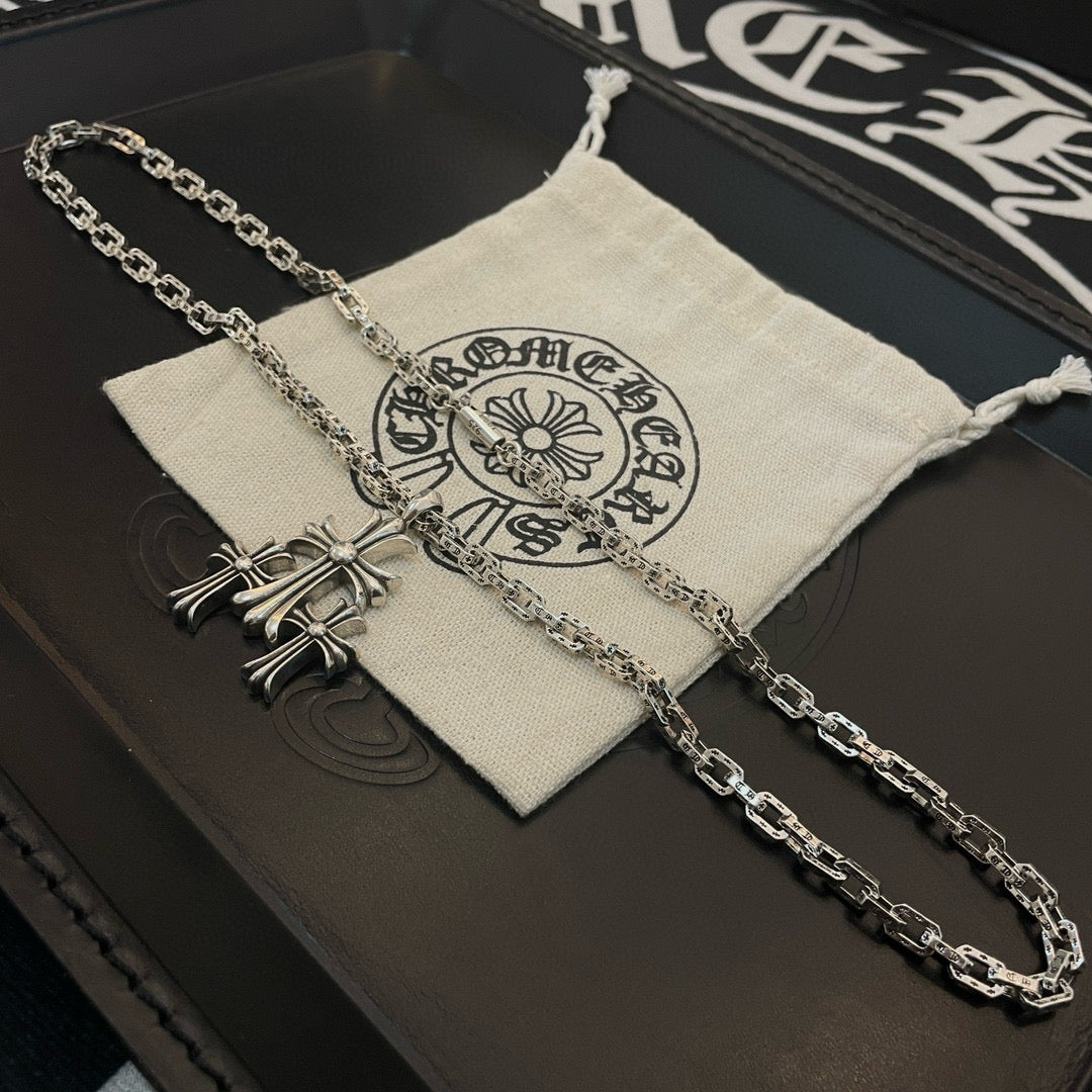 Silver cross pendant necklace draped over fabric pouch on black box