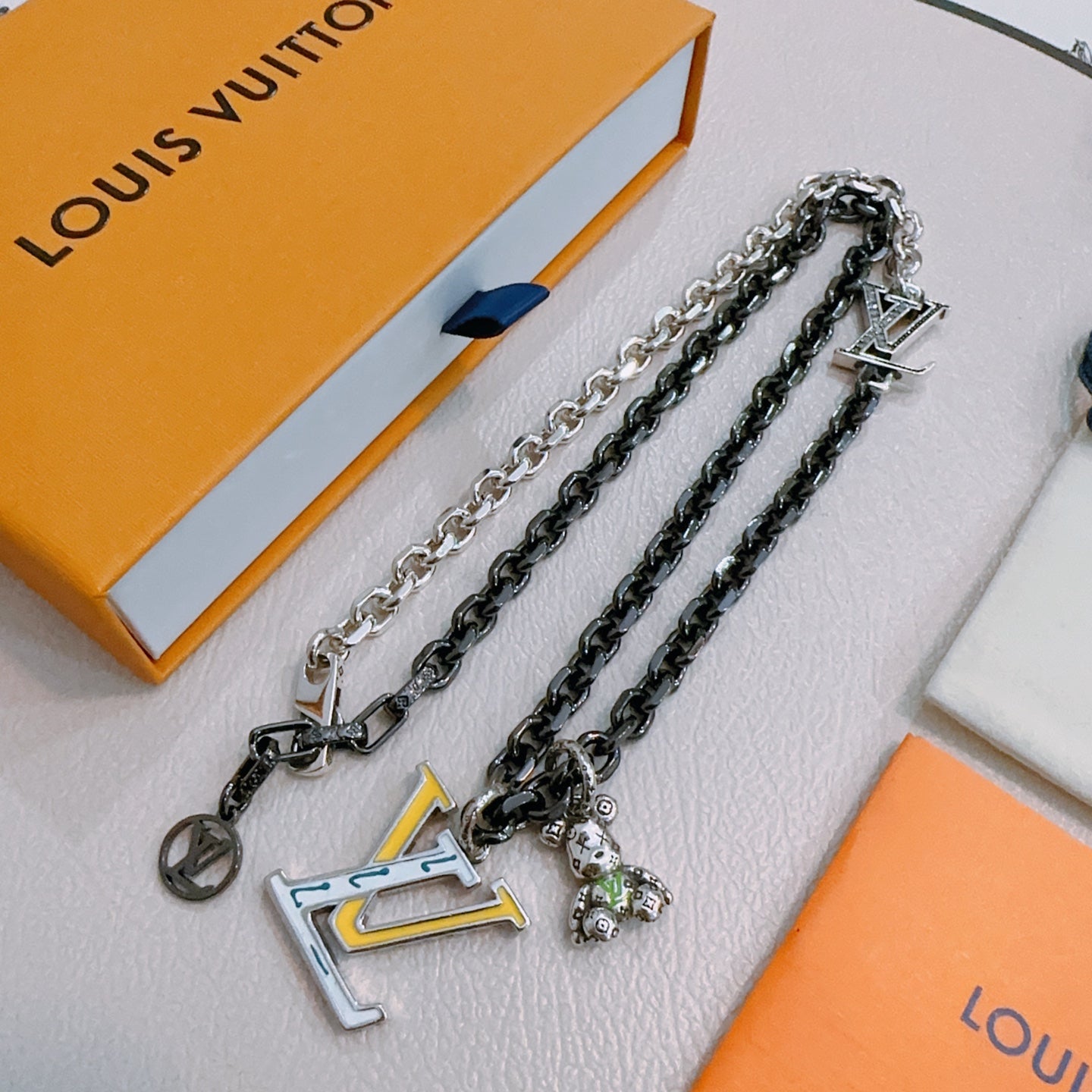 Louis Vuitton necklace set display, silver-tone and dark-tone chains with LV charm pendants
