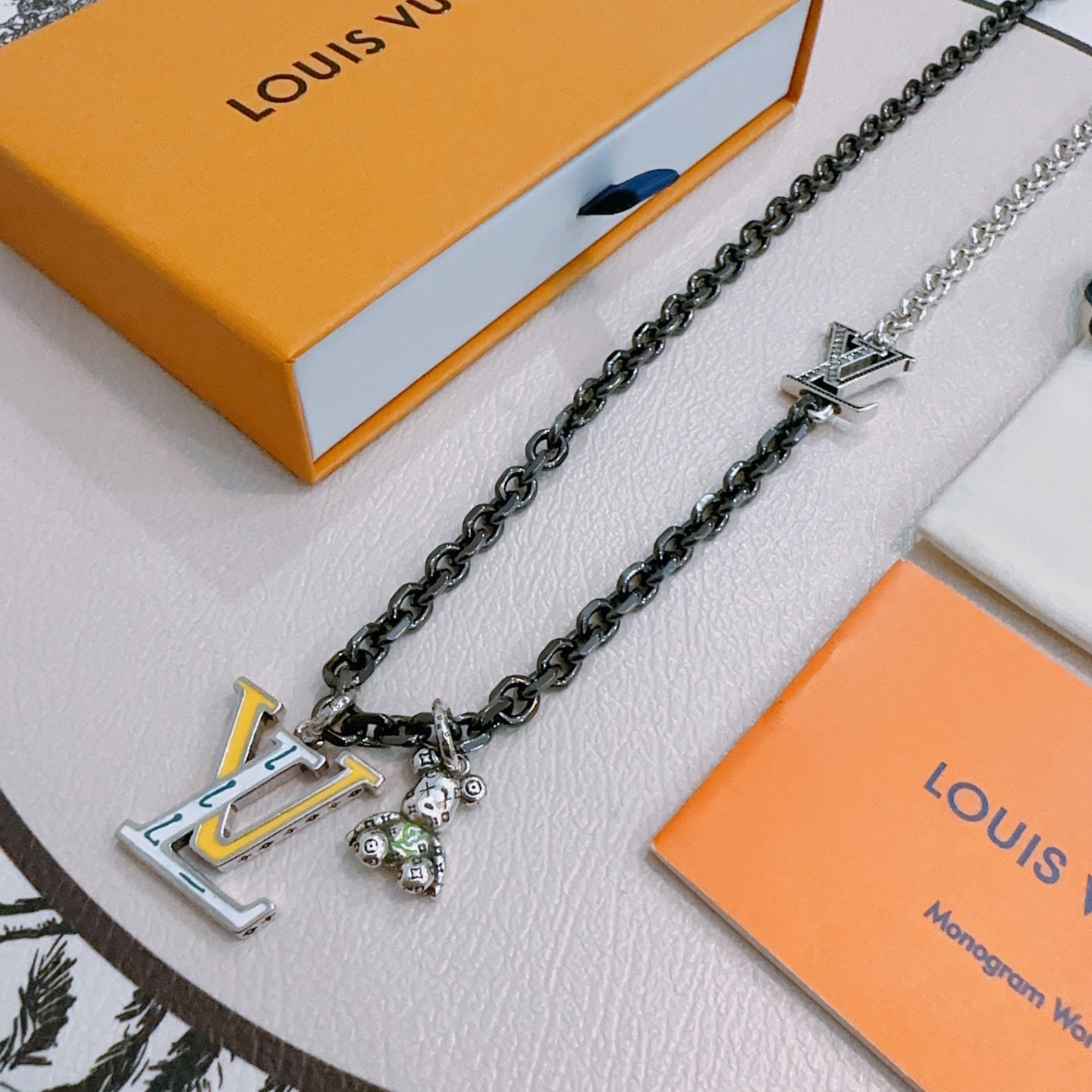 Louis Vuitton necklace display, dark-tone chain with LV charm pendant and bead detail
