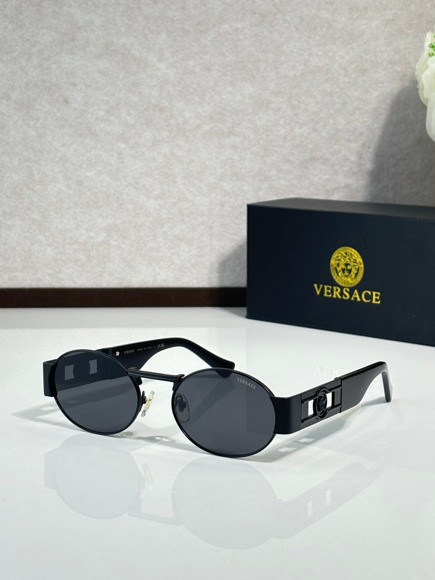 Round sunglasses with black frames and dark tinted lenses; gold-trim temple details.