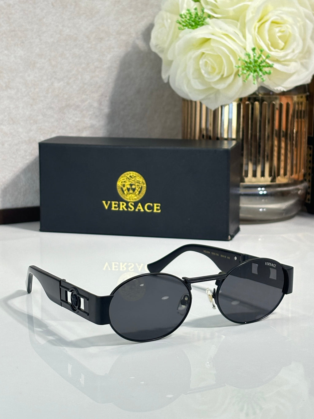 Round sunglasses with black frames and dark tinted lenses; gold temple accents.