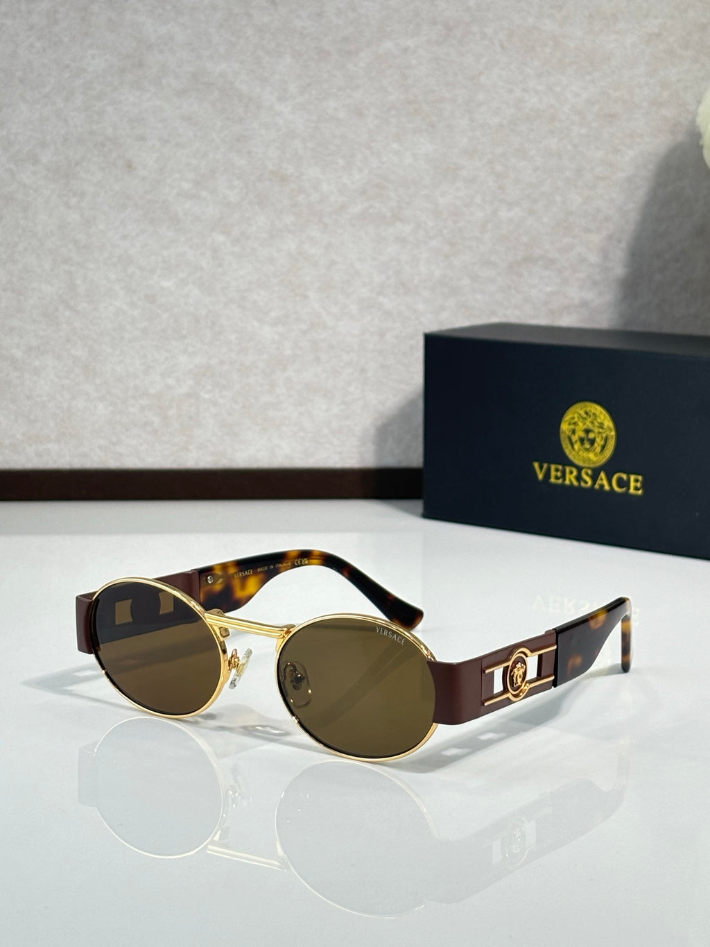 Round sunglasses with gold frames, dark lenses, and brown temple accents.