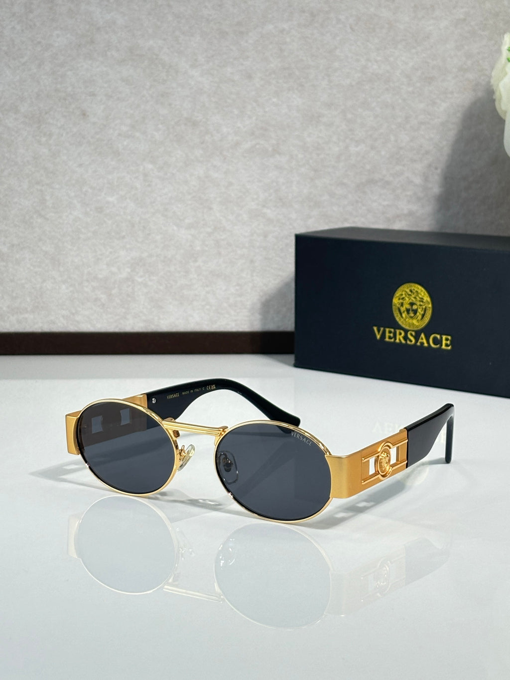 Round sunglasses with gold frames and dark tinted lenses; black temple accents.