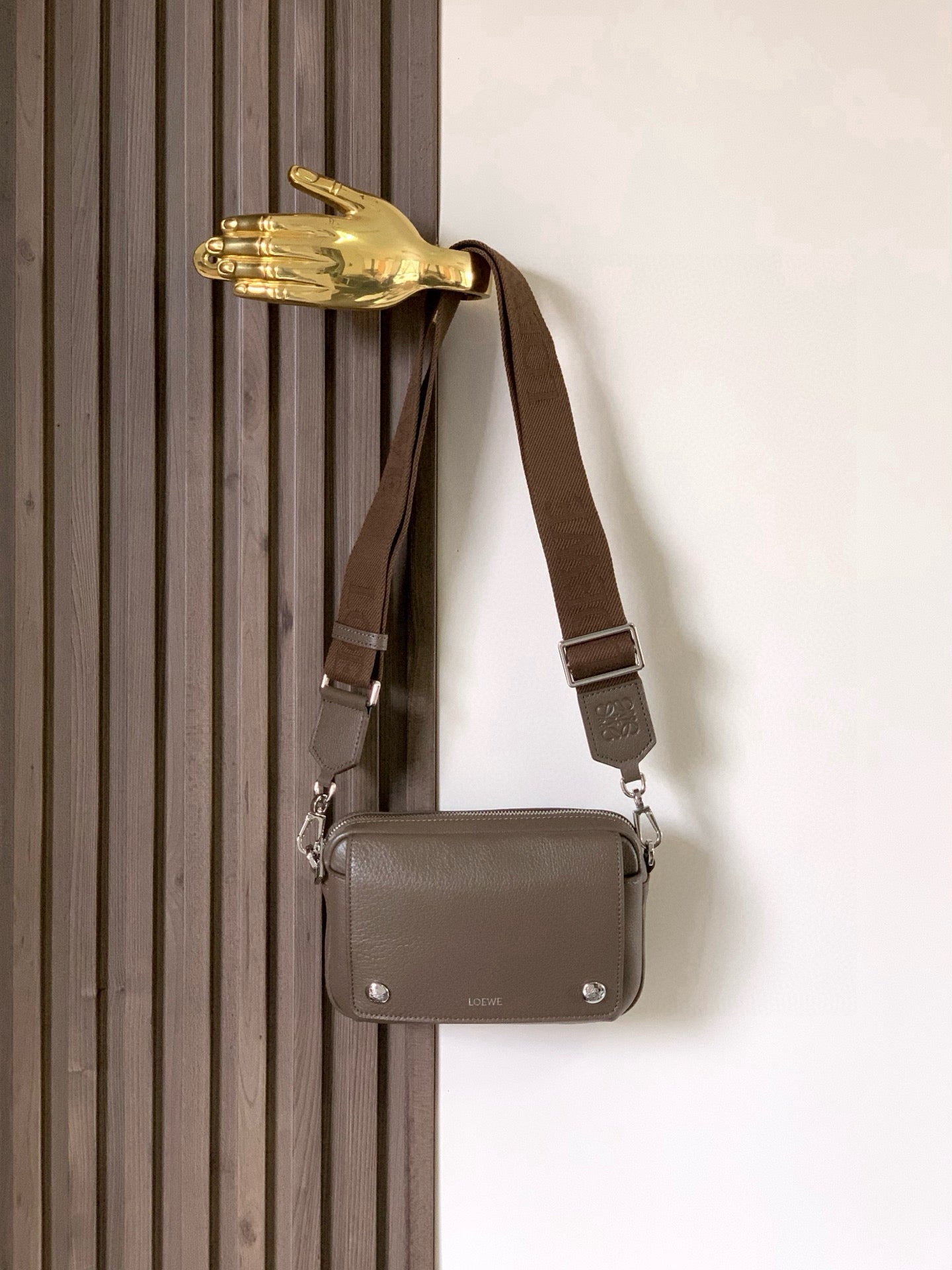Loewe men's taupe leather mini crossbody bag hanging from a shoulder strap