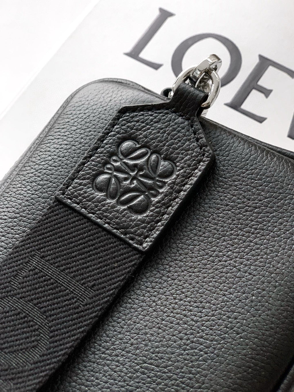 Men's leather crossbody bag close-up of embossed logo patch on dark textured strap