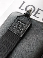 Men's leather crossbody bag close-up of embossed logo patch on dark textured strap