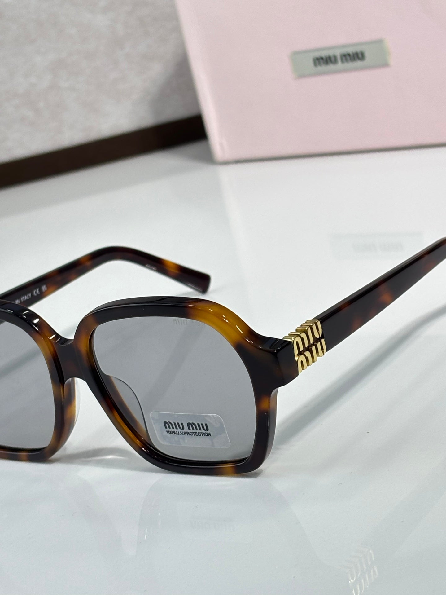 MiuMiu tortoiseshell eyeglasses close-up with dark lenses and gold logo bridge