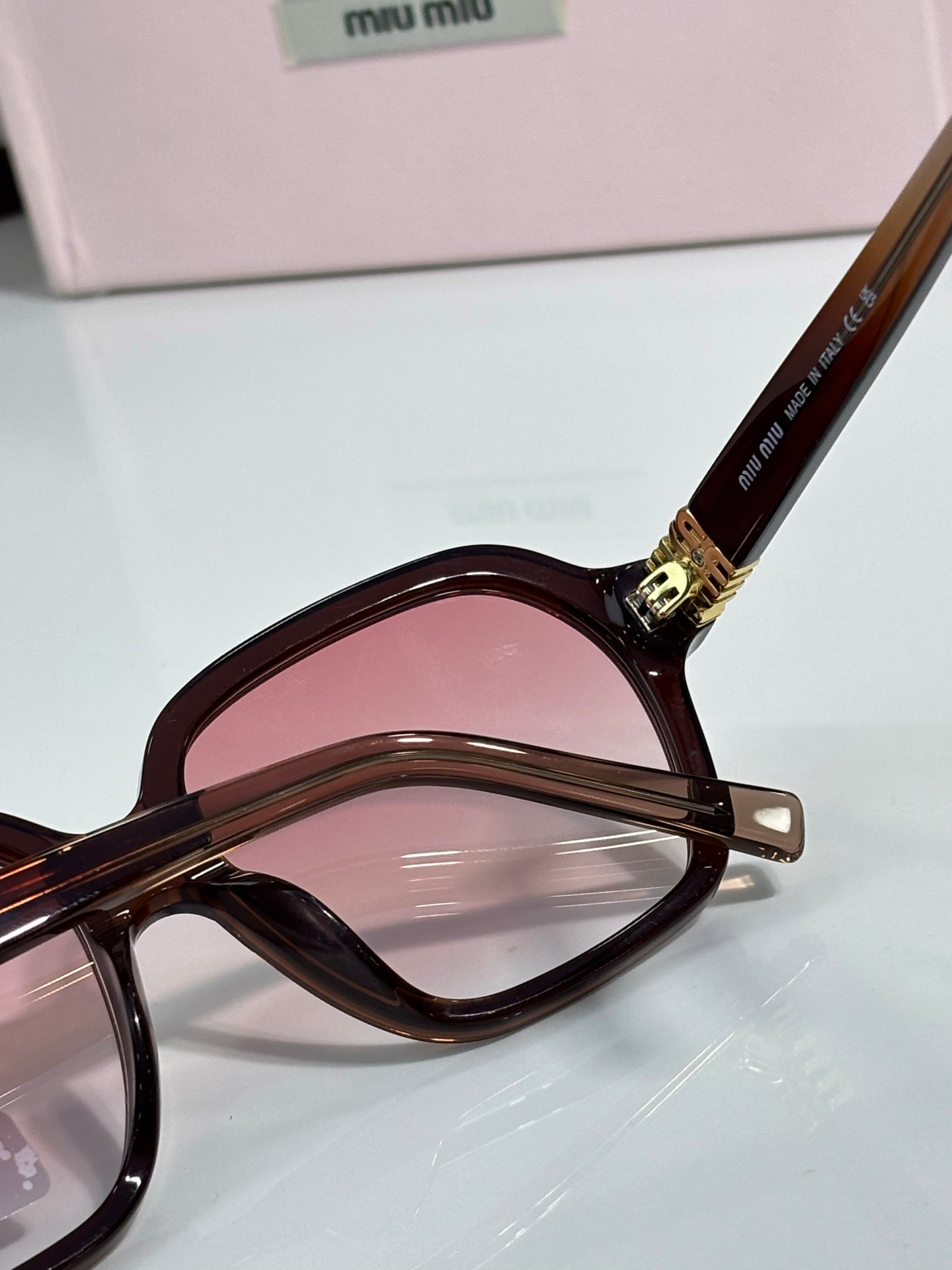 MiuMiu dark round eyeglasses close-up with pink-tinted lens and gold logo hinge