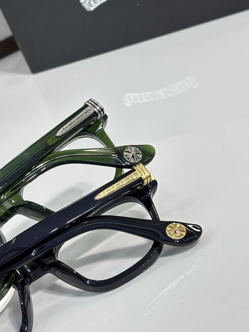 Stacked eyeglasses frames in dark green and navy with gold temple details