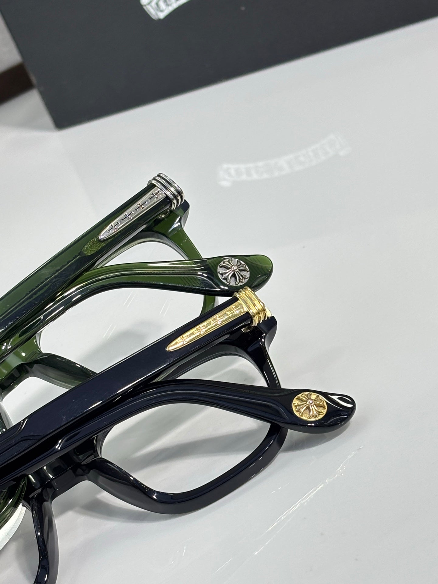 Stacked eyeglasses frames in dark green and navy with gold temple details