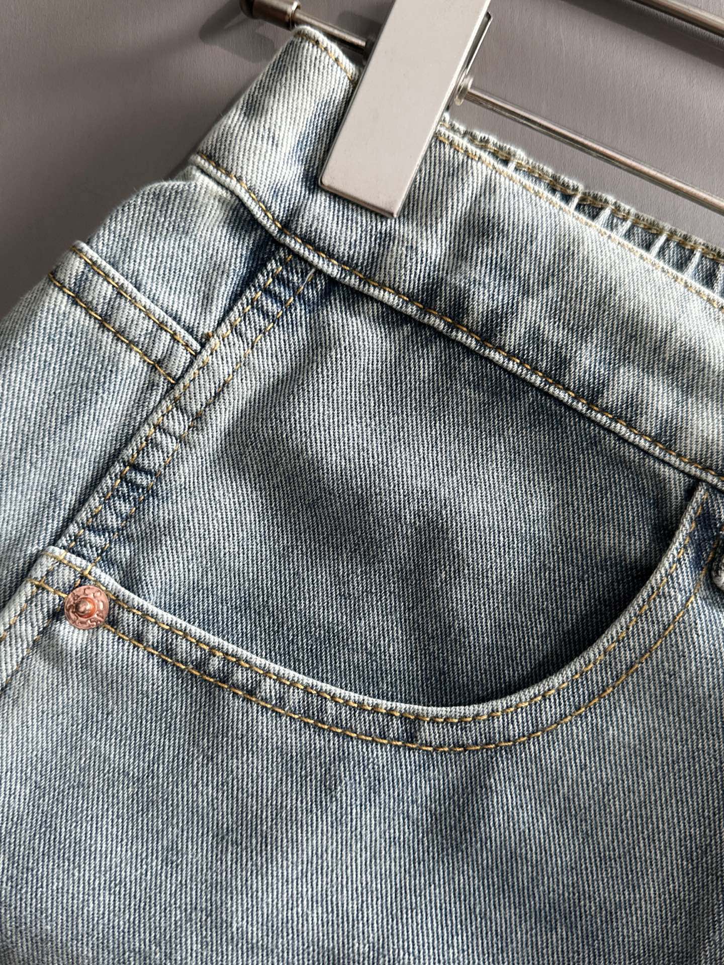 Light blue denim jeans close-up of waistband, stitched seams, and copper button
