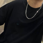 Silver chain necklace with small cross pendant on a black crewneck shirt