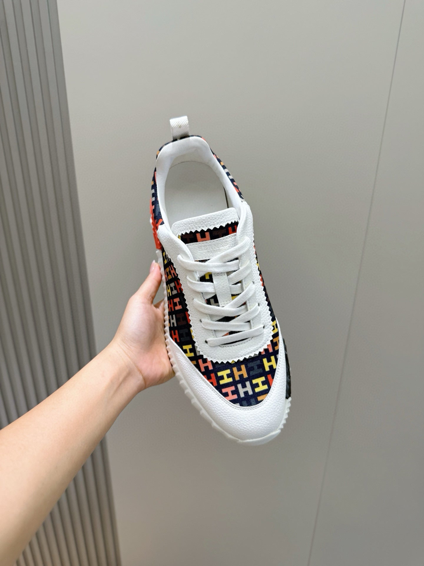 Hermes unisex sneaker close-up, heel and lace eyelets on logo-pattern upper