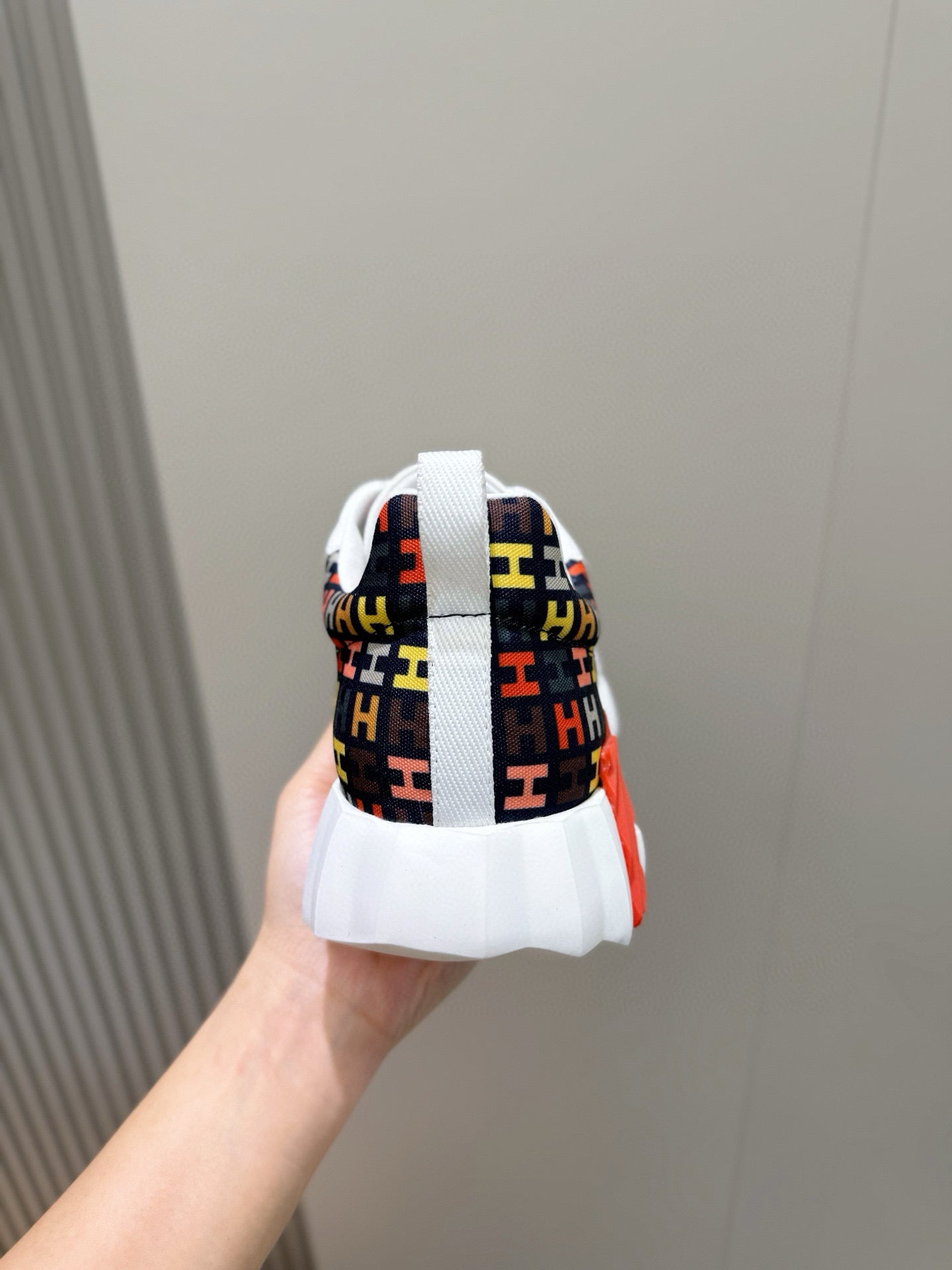 Hermes unisex sneaker back view, multicolor logo heel with white sole